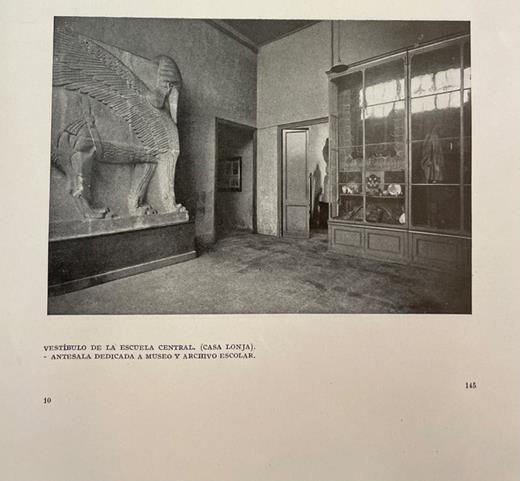 Photograph showing the plaster replica of the lamassu on a wooden pedestal against the wall. Moreover, there is a display case also on the wall, forming an angle with the replica, with other works acquired by the Royal Catalan Academy of Fine Arts of Sant Jordi. This room leads to the museum and the archive.