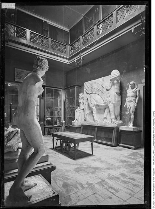 Early twentieth-century photograph of the hall of the Royal Catalan Academy of Fine Arts of Sant Jordi showing the location of various plaster copies of classical and Egyptian works and the lamassu, all of large dimensions, together with wall display cases containing smaller objects.